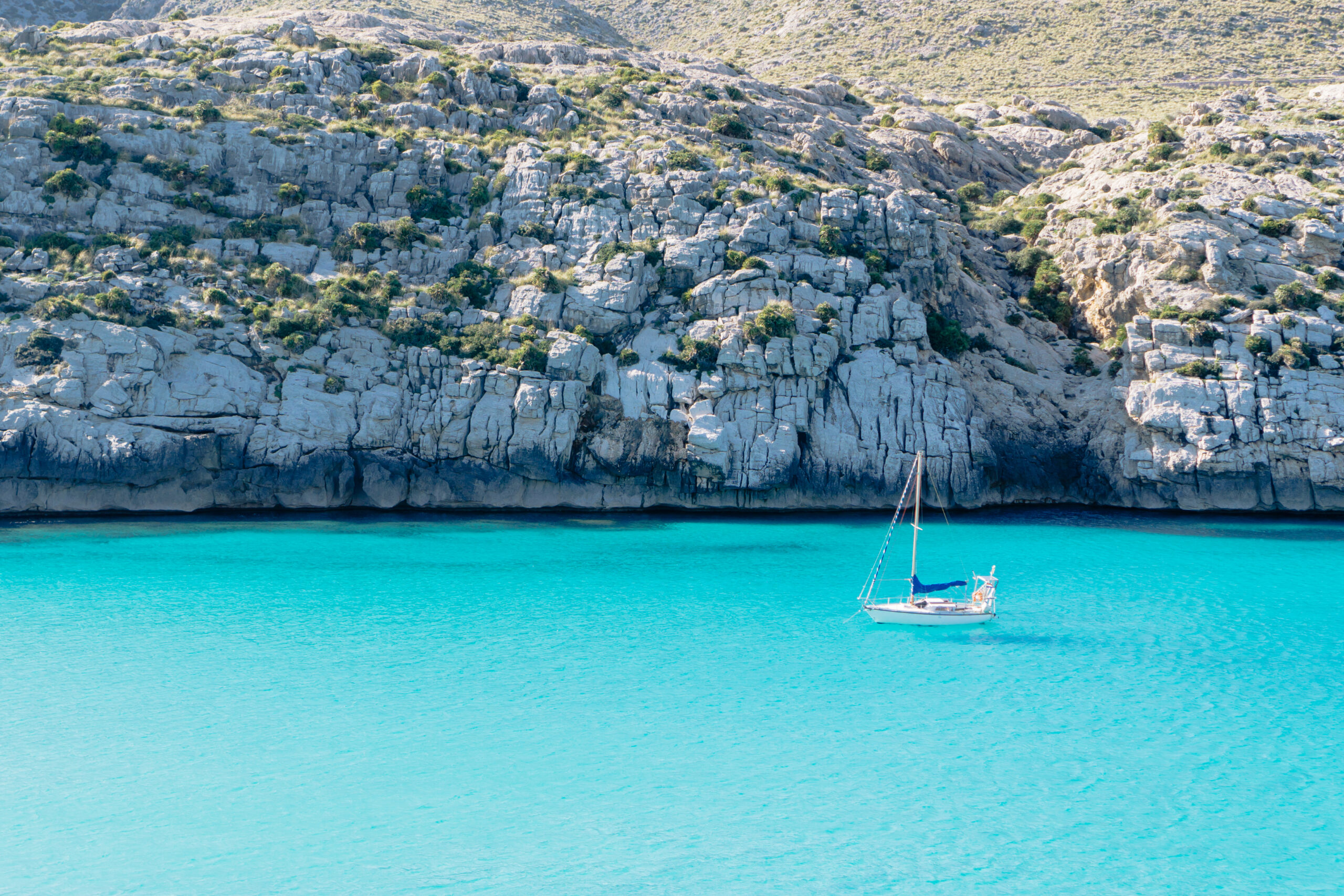 Voilier solitaire sur une eau turquoise dans les calanques entre Sanary et Cassis, falaises calcaires en arrière-plan