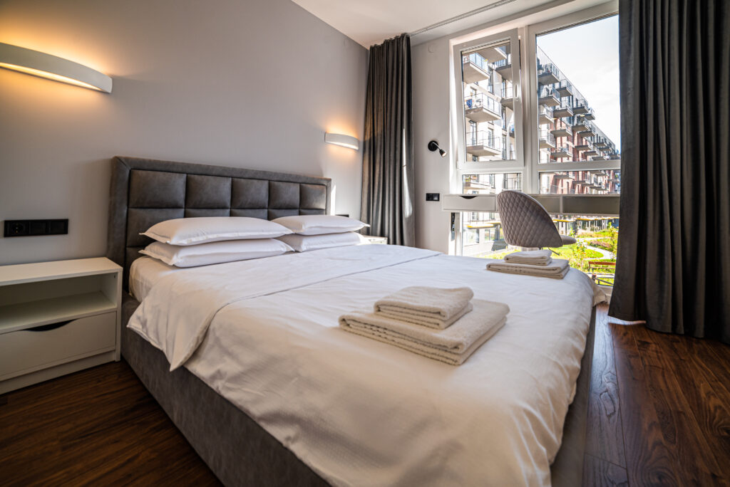 Chambre moderne aparthotel airbnb hôtel familial avec lit double, linge plié et grande fenêtre lumineuse.